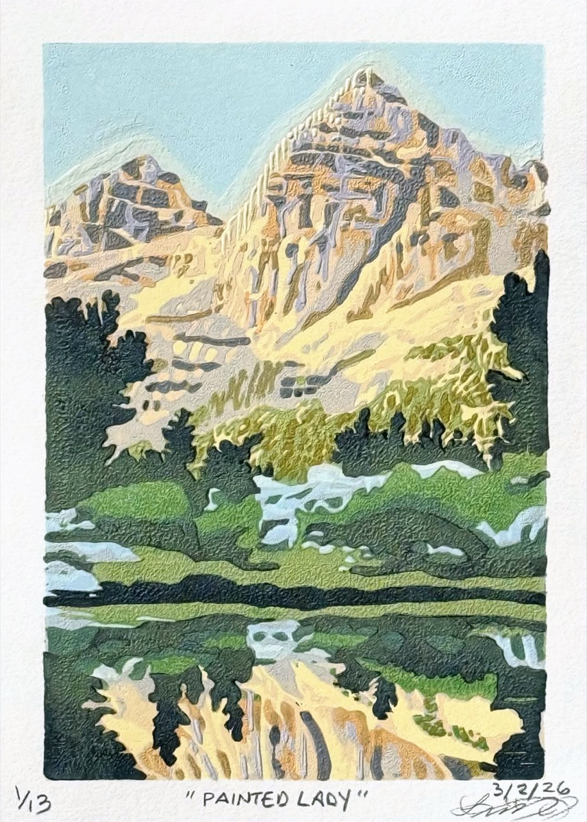 Painted Lady, the peak above Rae Lakes in Kings Canyon, banded pale and dark, with conifers along the shore and its summit repeated upside down in the still water.